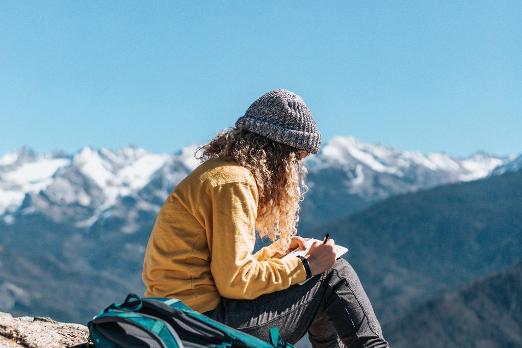 a young girl is writing in a notebook with the mountains in the background