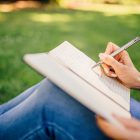 a girl writing in the notebook sitting on the grass