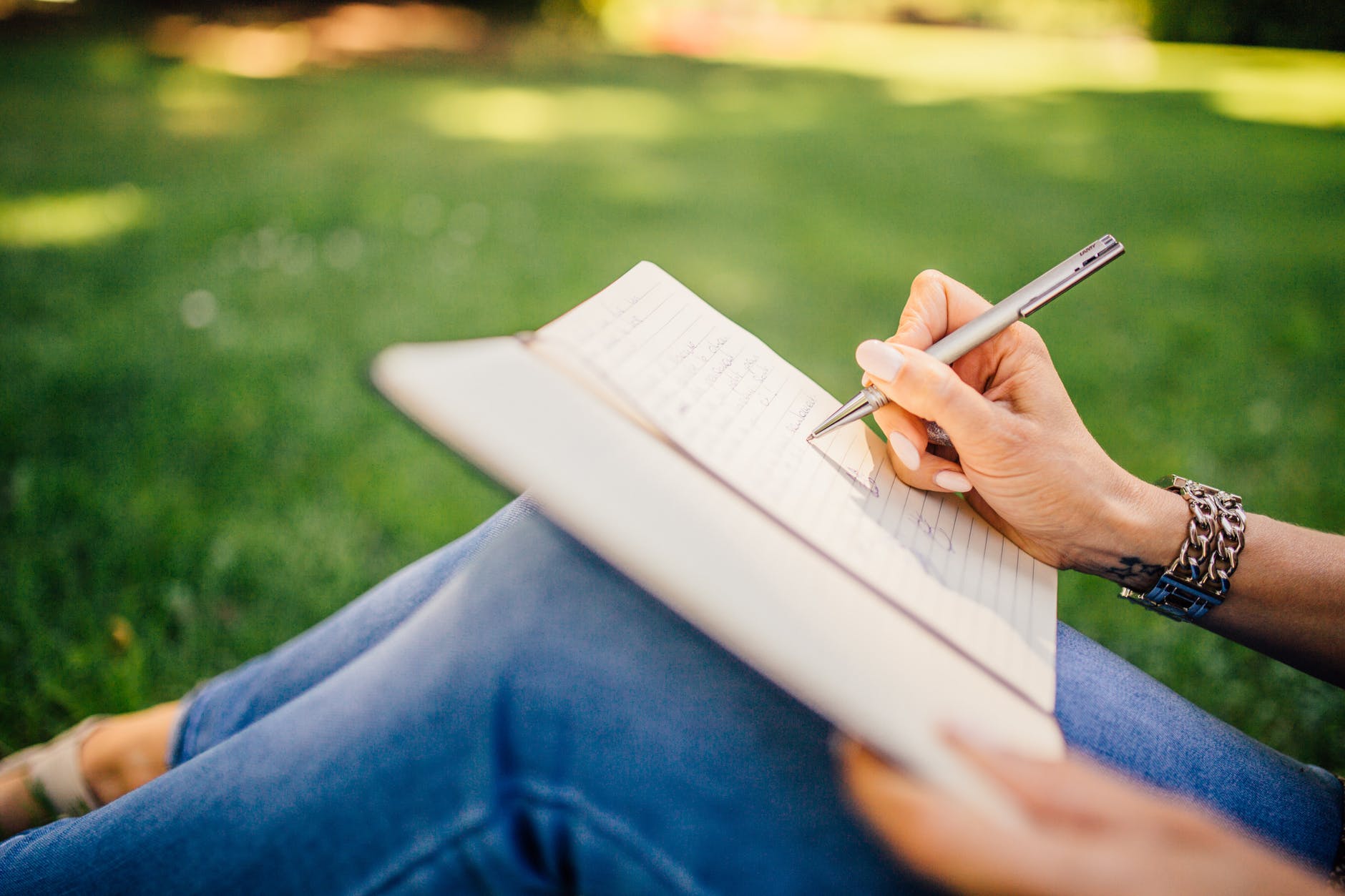 a girl writing in the notebook sitting on the grass