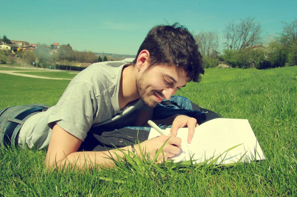 a man lies on the grass writing in the notebook