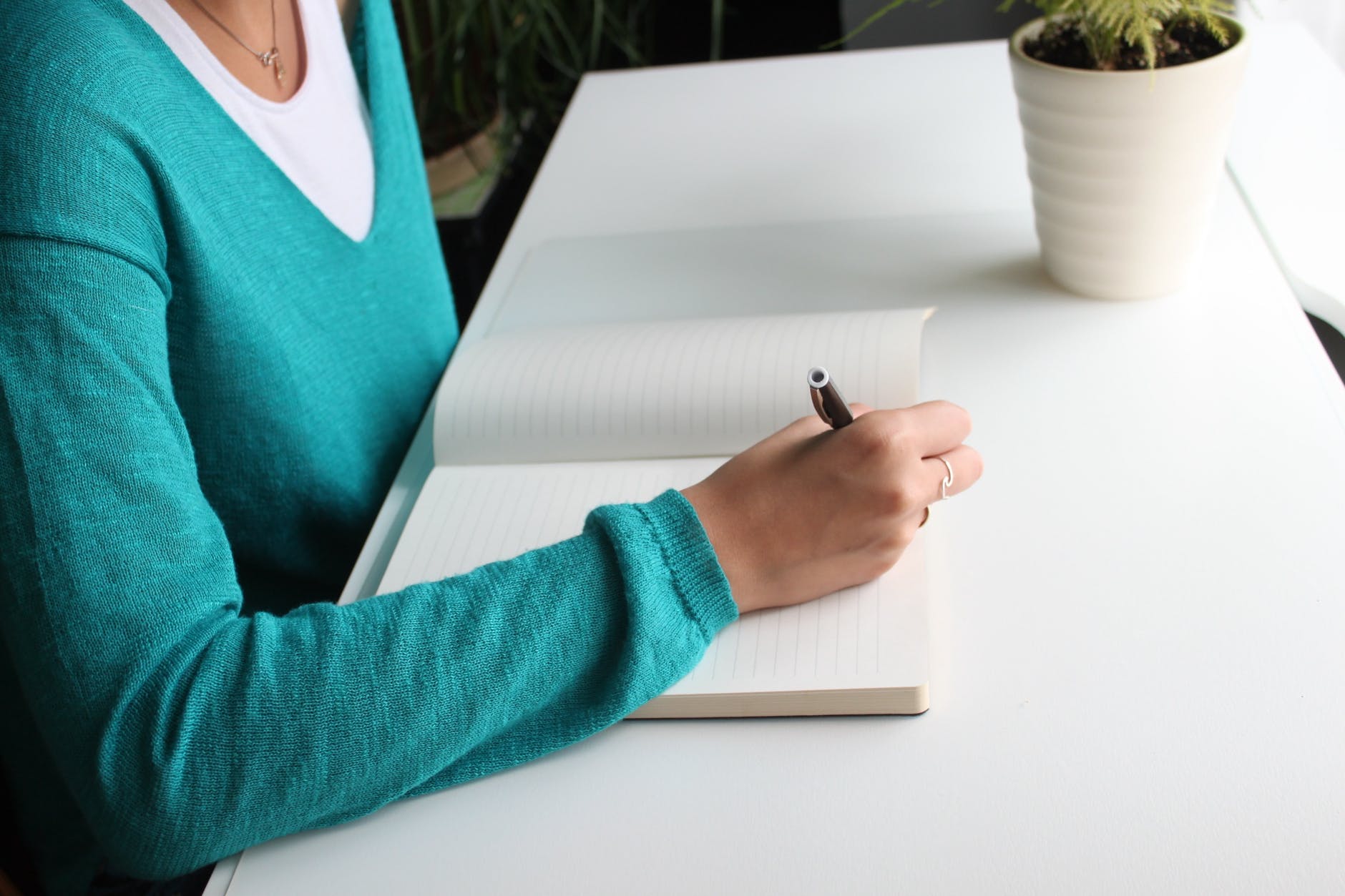 a girl in a blue sweater is writing in a notebook