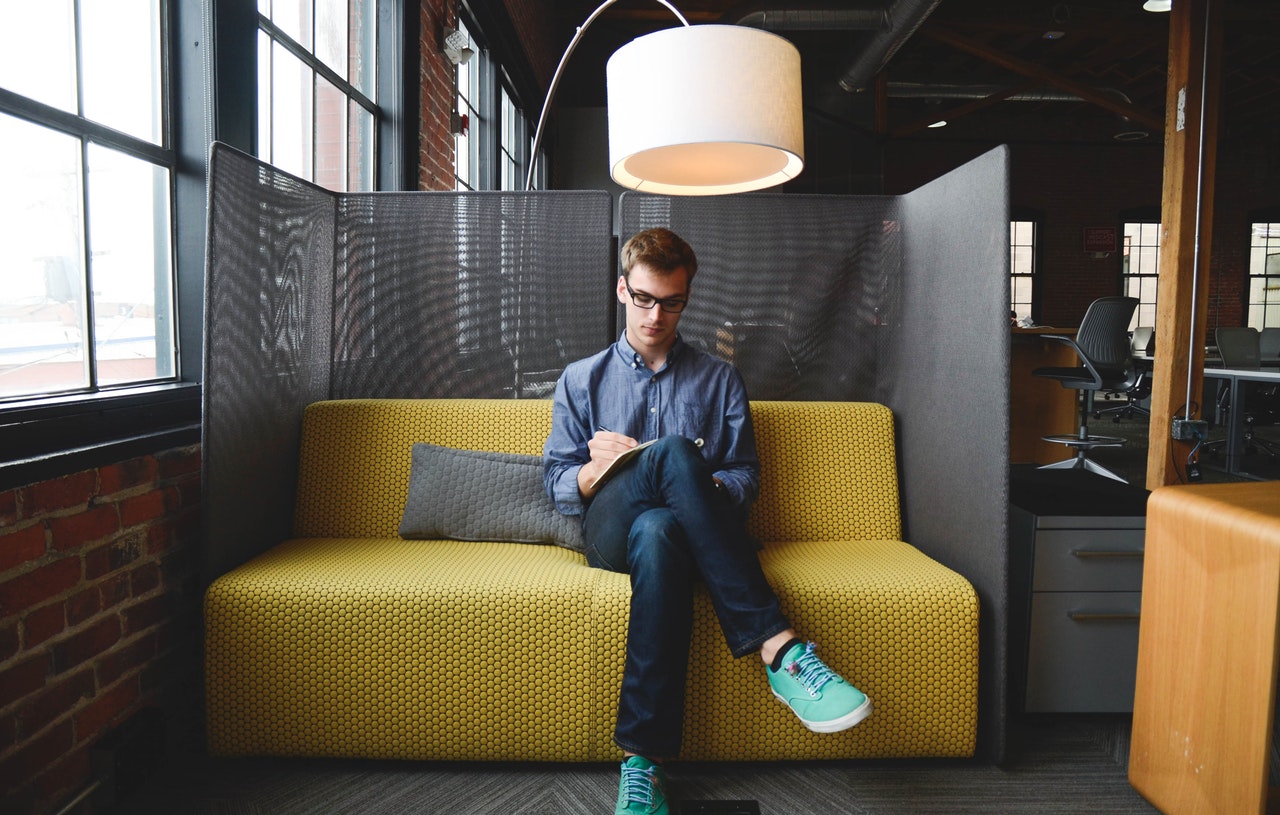 a guy is sitting on a couch and writing something in a notebook