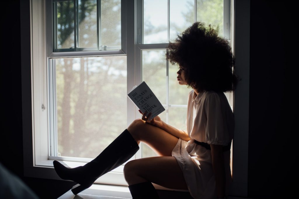 a girl sitting next to a window reading a book